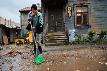 Image showing A woman diligently maintains the garden by collecting old, dry leaves, creating a picturesque scene of outdoor care and seasonal tidiness