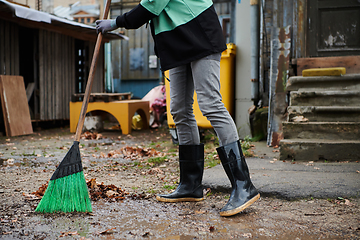 Image showing A woman diligently maintains the garden by collecting old, dry leaves, creating a picturesque scene of outdoor care and seasonal tidiness