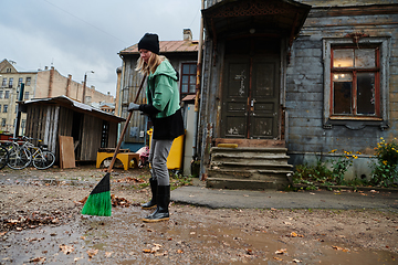 Image showing A woman diligently maintains the garden by collecting old, dry leaves, creating a picturesque scene of outdoor care and seasonal tidiness