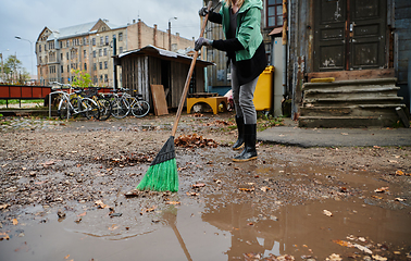 Image showing A woman diligently maintains the garden by collecting old, dry leaves, creating a picturesque scene of outdoor care and seasonal tidiness