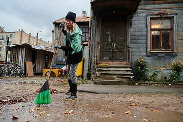 Image showing A woman diligently maintains the garden by collecting old, dry leaves, creating a picturesque scene of outdoor care and seasonal tidiness