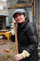 Image showing A woman diligently maintains the garden by collecting old, dry leaves, creating a picturesque scene of outdoor care and seasonal tidiness