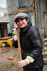 Image showing A woman diligently maintains the garden by collecting old, dry leaves, creating a picturesque scene of outdoor care and seasonal tidiness