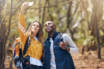 Image showing Selfie, happy couple and hiking adventure while holding phone for vacation travel memories in a forest or woods. Happy, love and exercise in healthy relationship with black man and white woman