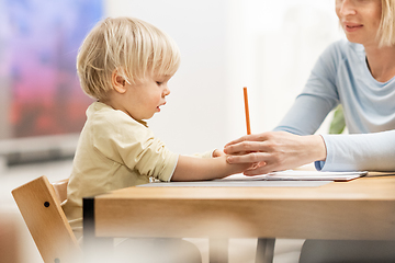 Image showing Caring young Caucasian mother and small son drawing painting in notebook at home together. Loving mom or nanny having fun learning and playing with her little 1,5 year old infant baby boy child.