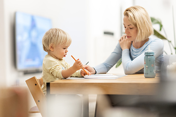 Image showing Caring young Caucasian mother and small son drawing painting in notebook at home together. Loving mom or nanny having fun learning and playing with her little 1,5 year old infant baby boy child.