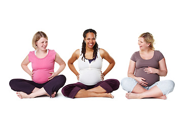Image showing Pregnant friends sitting against a studio white background, enjoying getting healthy and prenatal care together. Diverse mothers in a birth class, bonding and learning relax and stress relief tips