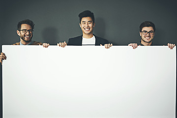 Image showing A group of young, smiling and professional business men holding a white sign copyspace portrait. A team of male designers standing together with a blank billboard for advertising or marketing