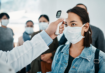 Image showing Covid screening with a female tourist in a mask having her temperature taken with an infrared thermometer while waiting to board in an airport. Travel restrictions during the corona virus pandemic