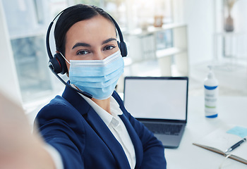 Image showing Customer support woman taking selfie during covid on phone while working on laptop and face mask. Receptionist or call center agent taking picture with smartphone camera at work during pandemic.