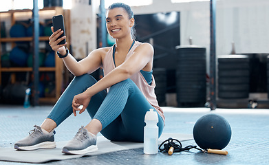 Image showing Woman taking selfie with phone after workout at the gym, reading social media post and relax after cardio fitness exercise at club. Athlete girl on mobile app for sports while training on floor