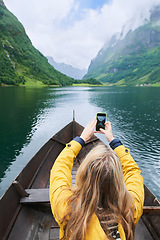 Image showing Adventure woman in row boat taking photo on smart phone of beautiful fjord lake for social media