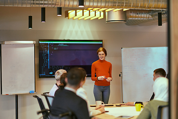 Image showing A pregnant business woman with orange hair confidently presents her business plan to colleagues in a modern glass office, embodying entrepreneurship and innovation