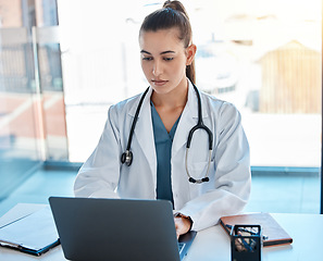 Image showing Doctor typing on a laptop in an office writing a proposal or on a video call using telemedicine. Young healthcare professional or GP using the internet for research or online consultation