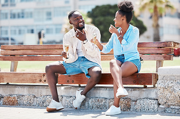 Image showing Happy black couple eating ice cream on a beach bench together, smiling while bonding and laughing. Young African American man and woman enjoying their summer romance, free time and relationship