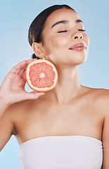 Image showing Grapefruit, woman skincare and wellness fruit for face grooming, wellness and diet health on a blue background in studio. Happy, smile and beauty brazilian model with vitamin c food product in hands