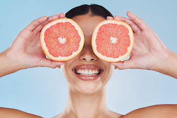 Image showing Grapefruit, woman skincare and face skin with fruit for wellness, health and facial on a blue background in studio. Happy, smile and beauty model with food product in hands hiding eyes with vitamin c