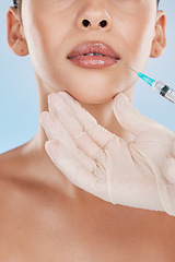 Image showing Closeup of a young woman getting lips injection treatment from a cosmetic doctor in a studio. Syringe and needle with lip filler for the mouth by a cosmetology beautician with a blue background.