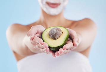 Image showing Hands holding an avocado fruit for skincare, beauty and cosmetic wellness on a blue mockup studio background. Woman with face mask for health, skin and body care giving nutrition food for eating