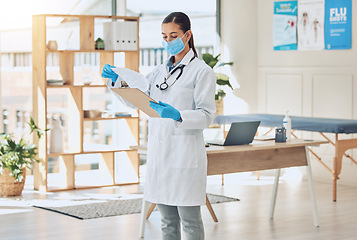 Image showing Medical doctor with a clipboard and face mask in her office reading covid results during pandemic. Young healthcare employee doing hospital paperwork in the clinic room in a medicare surgery center.