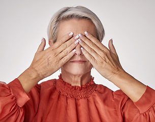 Image showing Senior, hands and covering eyes or face of mature woman suffering with a headache or eye strain while posing against a grey studio background. Elderly woman having problems with her vision or sight.