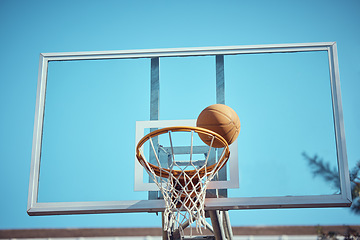 Image showing Basketball court, sport and hoop or ring net against a blue sky outside. Exercise, competitive and fun hobby for athletes with a ball on the basket for a goal with copy space or mock up outdoors