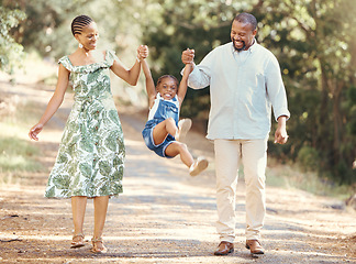 Image showing Happy parents swing girl at their hands in the forest during a walk in nature. Cheerful kid having fun while bonding with mother and father on family summer vacation or outing together in the woods