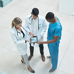 Image showing Group of doctors working on digital tablet while standing in the hospital hallway and talking. Top view of healthcare employees analyzing test results and treatment in medicare clinic with technology