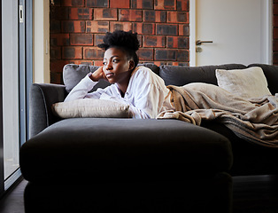 Image showing Bored, depression and isolation with black woman lying on her sofa during lockdown, quarantine or pandemic. Mental health, anxiety and stress with young female thinking and looking out her window