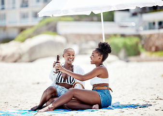 Image showing Friends relaxing and drinking a beer on the beach while on vacation together during summer. Happy black women making a toast with alcohol while sitting by ocean while on holiday in south africa.