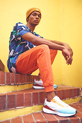 Image showing Black man, fashion and street style clothes on cool, trend or attitude model on steps by city wall background on building. Portrait of serious student sitting on stairs in urban punk clothing outdoor