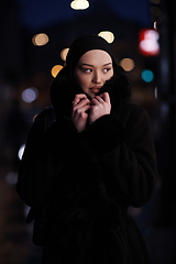 Image showing Muslim woman walking on an urban city street on a cold winter night wearing hijab