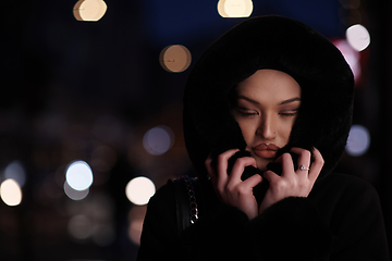 Image showing Muslim woman walking on an urban city street on a cold winter night wearing hijab