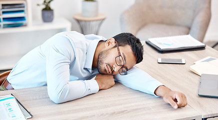 Image showing Burnout, sleeping and tired with an overworked business man asleep at his desk in the office. Exhausted, fatigue and dreaming with a young male employee napping on a table at work after working late
