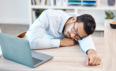 Image showing Tired, headache and sleeping worker behind laptop while lying his head on his desk in his office. Stress, burnout and chronic fatigue with young professional male feeling exhausted and overworked