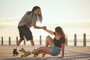 Image showing Help, falling and couple roller skating and holding hands at the beach in summer for a fun and healthy cardio activity. Friends love to skate and exercise on sidewalk as girl falls on the ground