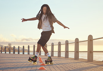 Image showing Roller skates, beach and sport with a man riding around training cone for fun, fitness and exercise at the seaside promenade. Hipster male athlete skating outside for leisure, health and recreation