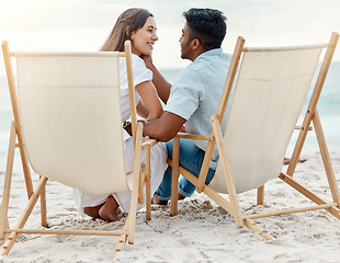 Image showing Couple, love and beach vacation of summer holiday with interracial lovers sharing a romantic moment while sitting on chairs in the sand. Happy and young man and woman on tropical honeymoon together