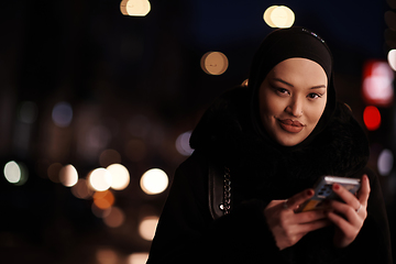 Image showing uropean Muslim Hijabi Business Lady checking her phone on urban city street at night