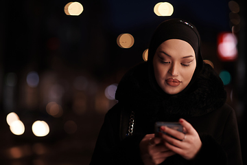 Image showing uropean Muslim Hijabi Business Lady checking her phone on urban city street at night