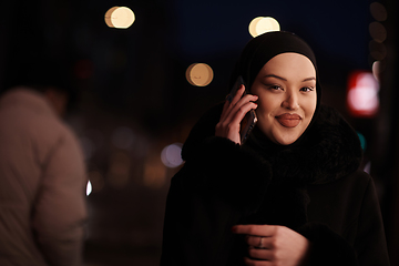 Image showing uropean Muslim Hijabi Business Lady checking her phone on urban city street at night