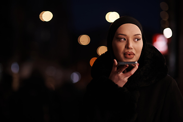 Image showing uropean Muslim Hijabi Business Lady checking her phone on urban city street at night
