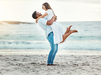 Image showing Man at beach lift woman with love, smile with sun setting over the horizon or background. Young couple travel to ocean on vacation, happy together with sunset over sea or waves in nature backdrop.