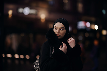 Image showing Muslim woman walking on urban city street on a cold winter night wearing hijab