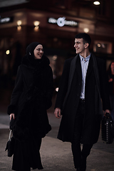 Image showing Happy multicultural business couple walking together outdoors in an urban city street at night near a jewelry shopping store window.