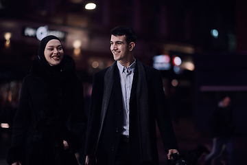 Image showing Happy multicultural business couple walking together outdoors in an urban city street at night near a jewelry shopping store window.