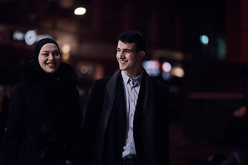 Image showing Happy multicultural business couple walking together outdoors in an urban city street at night near a jewelry shopping store window.