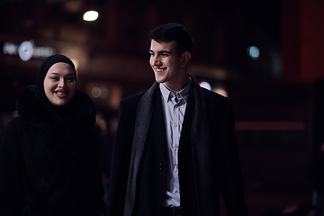 Image showing Happy multicultural business couple walking together outdoors in an urban city street at night near a jewelry shopping store window.