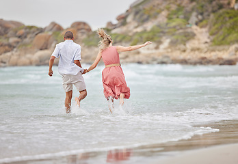 Image showing Interracial couple, ocean fun and holiday vacation together holding hands and enjoying the water. Man and woman bonding in a joyful relationship for beach time, waves and nature in the outdoors