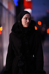 Image showing Muslim woman walking on an urban city street on a cold winter night wearing hijab